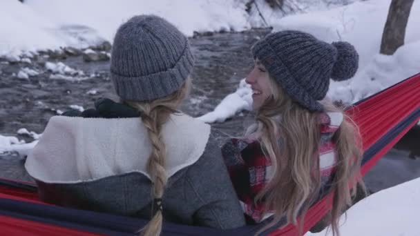雪の中で冬の間 川の隣のハンモックに座っている2人の女性 — ストック動画