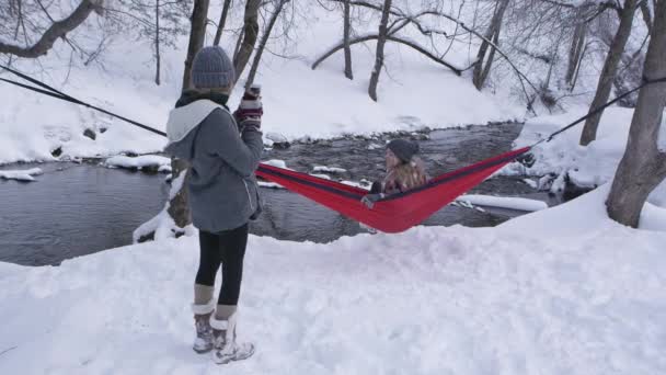 姐姐在河边拍照时 女孩穿着吊床在雪地里摆姿势拍照 — 图库视频影像