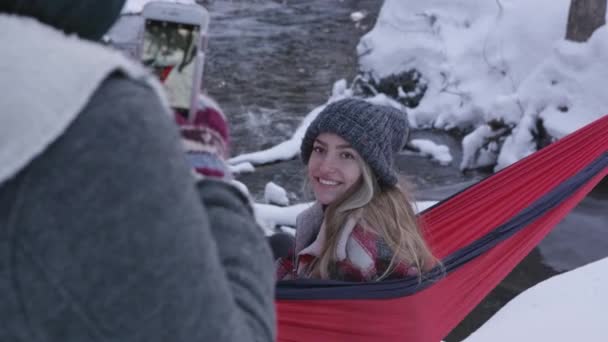 当姐姐在外面的雪地里坐在吊床上给男人拍照时 女孩笑着拍照 — 图库视频影像