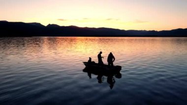 Gün batımında teknede balık tutan balıkçıların silueti. Hebgen Gölü 'nde balık tutmaya çalışan biri gibi..