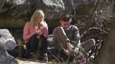 Genç bir kadın ve adam kaya tırmanışına hazırlanırken ayakkabılarını giyer ve konuşurlar..