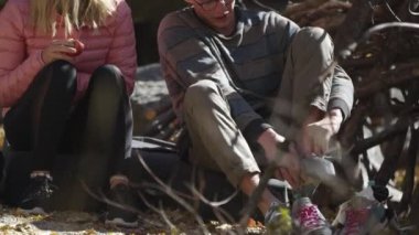 Genç bir adam ve kadın kaya tırmanışı ayakkabılarını giyip kayaya tırmanmaya hazırlanırken konuşuyor..