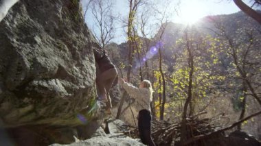 Genç bir kadın, erkek düşerse diye kollarını kaldırarak spor olsun diye kayaya tırmanıyor..