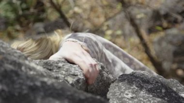Genç bir kadın kayayı kavramak için uzanır ve kayalar üzerinde tırmanır..