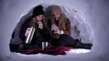 Igloo 'da oturan ikiz kardeş birbirleriyle konuşurken fincanlara sıcak çikolata döküyorlar..