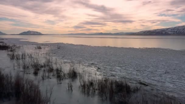 ユタ州の冬の間 凍結した湖の海岸線を越えて日没に向かって飛ぶ — ストック動画