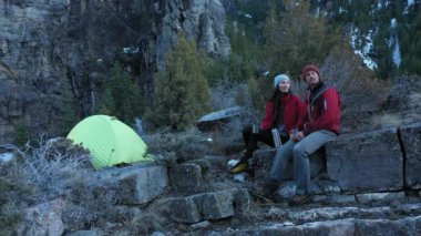 Uçurumun kenarında oturan bir çift adam uzaktaki bir yeri işaret ediyor ve kamp alanından manzara hakkında konuşuyorlar..