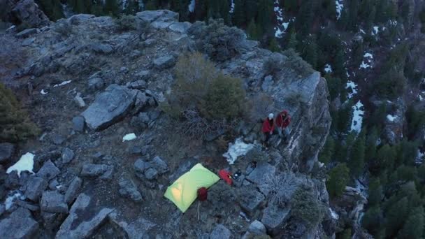アメリカのフォークキャニオンを見下ろす崖の上のキャンプ場の空中ビューカップルは夕暮れ時に棚の上に座っています — ストック動画