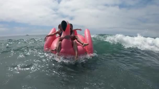 年轻女人骑着粉红火烈鸟在海滩上把玩具炸飞 随波逐流 把玩具推向岸边 — 图库视频影像