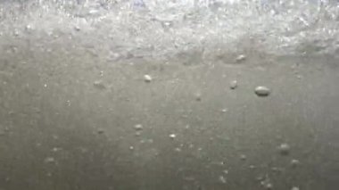 Dalgalar kameraya çarparak suyun üstünde ve altında kum ve suyu karıştırıyor..