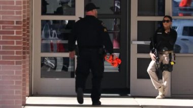 Ekim 2019, Highland Utah: Kilit altında liseye giriş yapan kadın memur, elleri havada öğrenciler tahliye edilirken arka planda yürüyorlar.