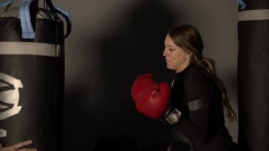 Genç bir kadın boks yapmayı öğrenirken torbaya yumruk atıyor..