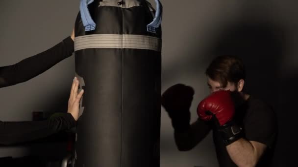Mulher Apoiando Saco Perfuração Como Homem Bate Com Luvas Boxe — Vídeo de Stock