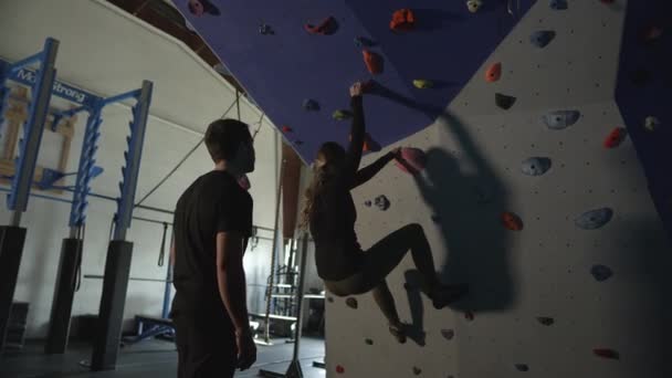Жінка Піднімається Скелястою Стіною Спортзалі Чоловік Заохочує Помічаючи Безпеки — стокове відео