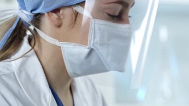 Laboratuvarda çalışan kadın hemşire yüzünü maske ve kalkanla örtüyor..