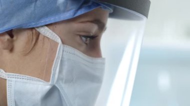 Laboratuvarda maske takıp kalkan takan kadın hemşirenin yan görüntüsü..