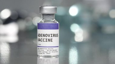 Laboratuvarda Adenovirüs aşısı şişesi. Yanında şırıngayla şişenin etrafında dolaşıyor..