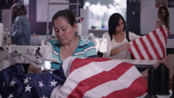 Dikiş atölyesinde çalışan farklı etnik kökenlere sahip kadınların Amerikan Bayrakları 'nı oluşturması.