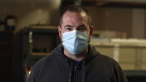 Koronavirüs salgını sırasında kameraya bakan yüz maskesi takan bir erkek..