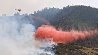 Airplane dropping fire retardant on wildfire burning on mountain above Provo Utah on July 31st, 2019. clipart