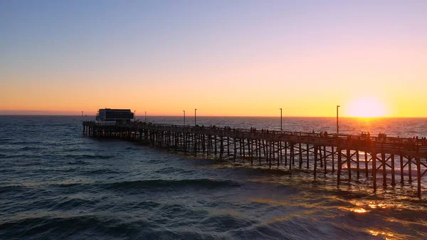 Günbatımında Newport sahil iskelesinin geniş hava manzarası plajda geriye doğru hareket ediyor..