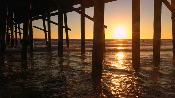 Panning Uitzicht Zonsondergang Onder Pier Als Golven Rollen Het Strand Rechtenvrije Stockafbeeldingen