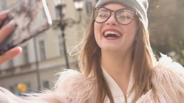 Uśmiechnięta kobieta, biorąc zdjęcie siebie w miejskich ulic. Piękna brunetka dziewczynka kaukaski w białą kurtkę z sprawia, że selfie. Turysta. — Wideo stockowe