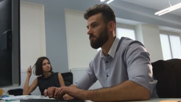 Joven hombre de negocios trabajando en su portátil, mientras sus colegas hablan entre sí . — Vídeo de stock