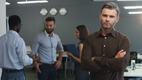 Hombre de negocios guapo sonriendo en cámara, mientras sus socios discuten nuevo proyecto . — Vídeo de stock