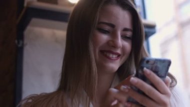 Kafede kahve içme telefon üzerinde app gülümseyen kullanan akıllı kız. Güzel çok kültürlü genç casual kadın profesyonel üstünde hareket eden telefon.