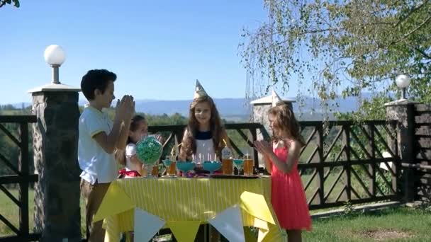 Cinco niños pequeños se sientan en la mesa amarilla con pastel en la fiesta de cumpleaños. Inscripción Feliz cumpleaños en la pared — Vídeo de stock