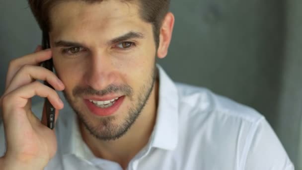 Sharing good news. Side view of handsome young man talking on the mobile phone and smiling while sitting at his working place in office — Stock video