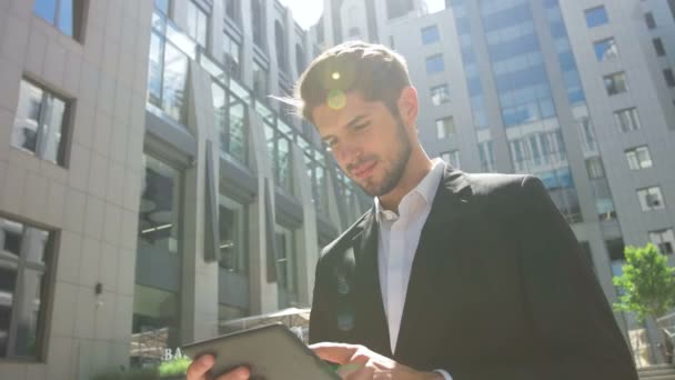 Young man using his tablet in front of a business center. — Stockvideo
