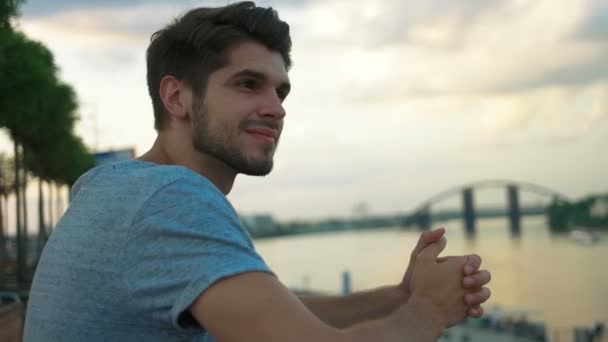 Молодий чоловік розслабляється перед красивою блакитною річкою . — стокове відео