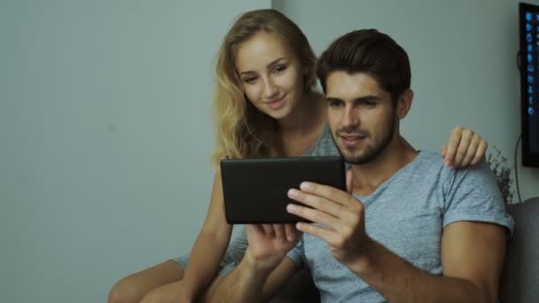 Gelukkige jonge paar met behulp van een tablet, gekleed in modieuze shirt op een bakstenen muur achtergrond — Stockvideo