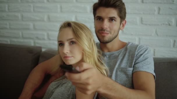 Pareja asombrada viendo el programa de televisión sentado en un sofá en casa — Vídeos de Stock