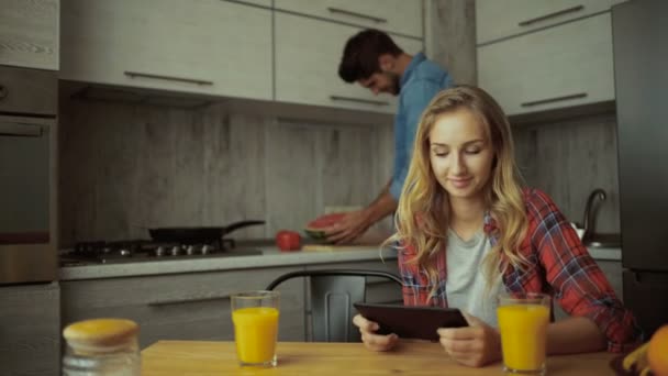 Mujer joven usando tableta, hombre cortando sandía . — Vídeos de Stock