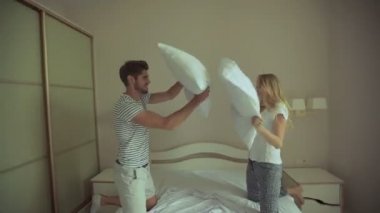 Mutlu çift yastık sahip otel odasında mücadele. Onlar iç çamaşırı giymek ve yatakta bendend dizlerinin üzerinde durmak. Herkes bir yastık tutuyor. Kadın uzun sarışın saçlı, adam siyah kısa saçlı.
