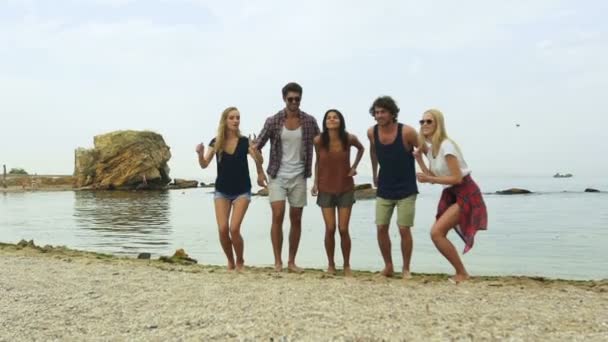 Vista trasera de un grupo de amigos saltando en el aire en la playa — Vídeo de stock