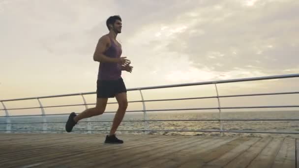 Young smiling handsome man running on beautiful beach in summer. — Stock Video
