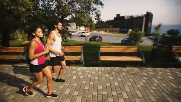 Twee jonge mensen opleidingen voor de marathon op prachtig park in de buurt van de zee. — Stockvideo