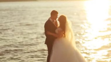 Şık takım elbise ve güzel gelin nehir önünde öpüşme beyaz lüks gelinlik giyen genç damat.