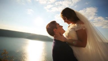 Ellerinin üstünde güneş ışığı onun güzel genç gelin taşıyan ve gülümseyen, dağın kalırken şık mutlu damat.