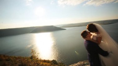 Ellerinin üstünde güneş ışığı onun güzel genç gelin taşıyan ve gülümseyen, dağın kalırken şık mutlu damat.