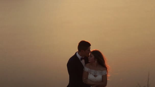 Hermosa novia con elegante vestido blanco besando a su marido en la colina de la montaña . — Vídeos de Stock