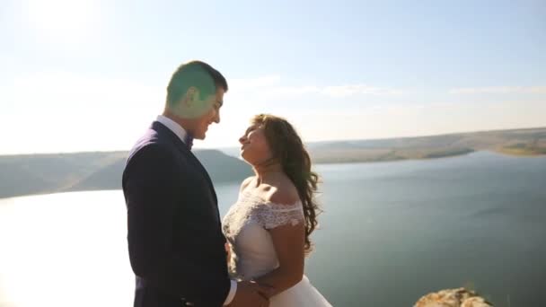 Schöne fabelhafte glückliche Braut und stilvoller Bräutigam umarmen sich vor dem Hintergrund der sonnigen atemberaubenden Berge. — Stockvideo