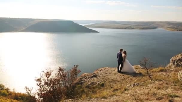 Θαυμάσιο η όμορφη νύφη χαρούμενος και κομψό γαμπρό αγκάλιασμα στο φόντο του sunny εκπληκτικά βουνά. — Αρχείο Βίντεο
