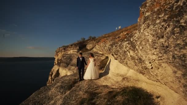 Şık genç damat tutarak el ve güzel gelini dağların muhteşem manzaralı, öpüşme. — Stok video