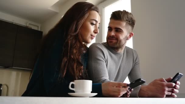 Hombre guapo y su novia usando teléfonos en la cocina . — Vídeo de stock