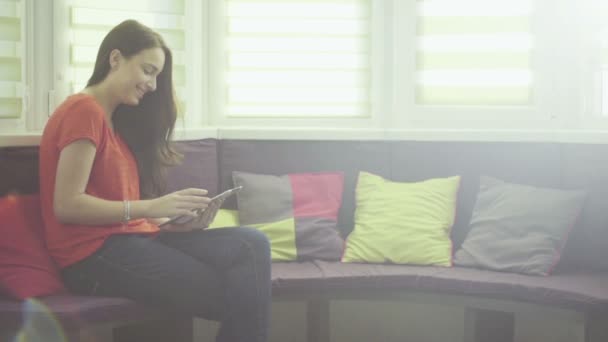 Junge hübsche Kaukasierin sitzt auf einer Couch im Wohnzimmer und benutzt ein Tablet. — Stockvideo